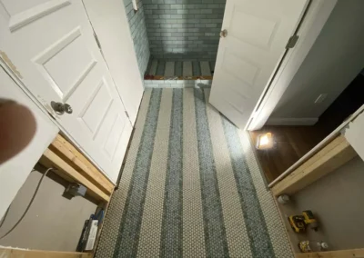 Bathroom under renovation with white and blue tile flooring, partially open doors, and a shower area with blue subway tiles.