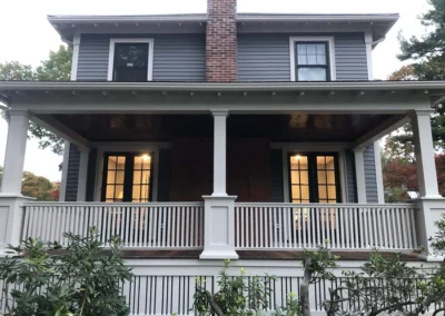 Front view of a two-story house with custom carpentry, featuring a covered porch and detailed railing.