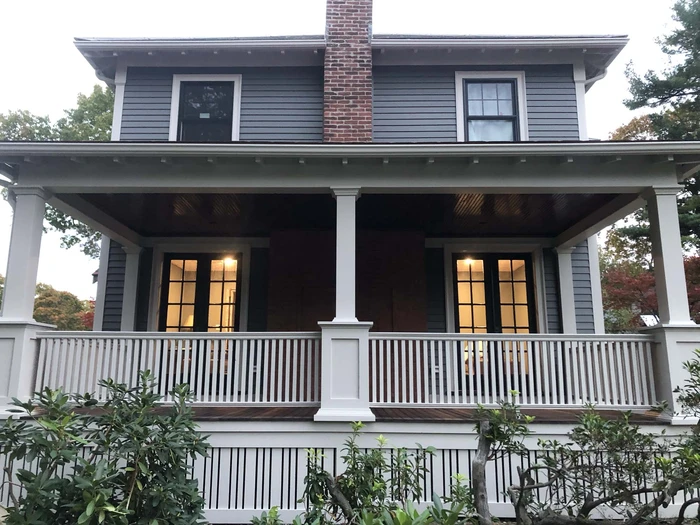 Front view of a two-story house with custom carpentry, featuring a covered porch and detailed railing.