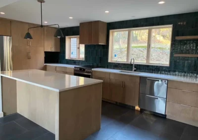 Modern kitchen with wooden cabinetry, white countertops, and a green tile backsplash.
