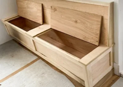 Built-in wooden bench with open storage compartments under the lid, located by a window.