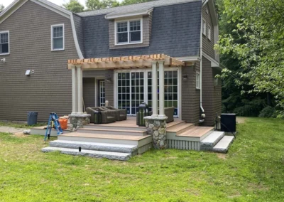 A house with a newly built wooden deck and pergola, featuring stone pillars and outdoor seating.