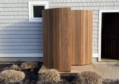 Wooden outdoor shower enclosure attached to a residential house with light gray siding.