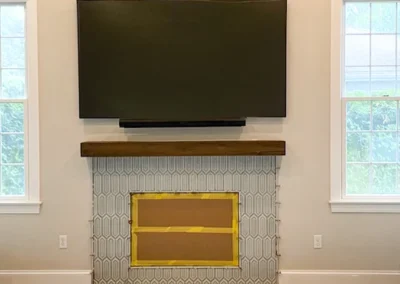 TV mounted above a mantel, unfinished fireplace area below, between two windows.