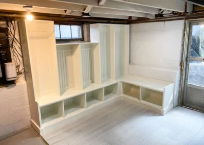 White L-shaped bench with cubbies in a basement corner, under an exposed ceiling with a single bulb.