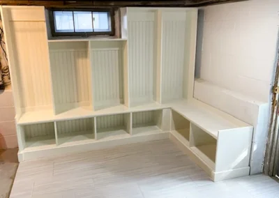 White built-in storage with shelves in a basement, beneath a small window.