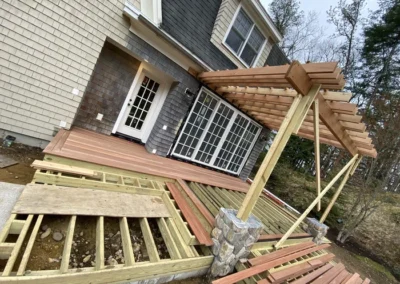 A partially constructed wooden deck with pergola and stone pillars attached to a house with sliding glass doors.