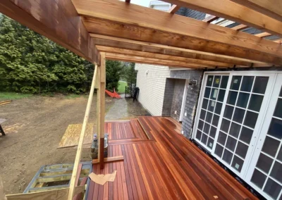 Wooden deck under construction with a pergola frame, adjacent to a house with large glass doors.