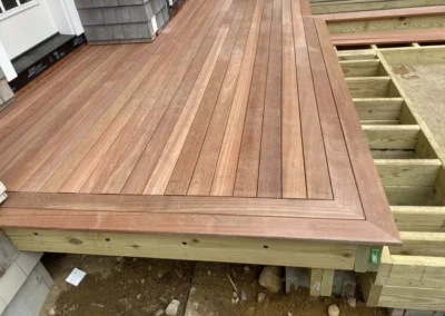 Wooden deck under construction with custom carpentry featuring wooden planks laid in a herringbone pattern, partially finished with visible support beams.