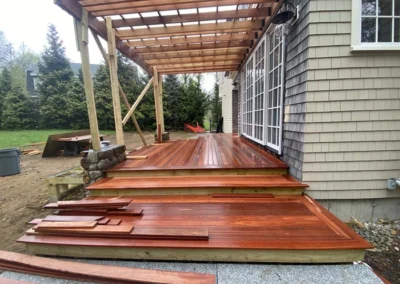A newly constructed wooden deck attached to a house, featuring a pergola and steps. The wood has a rich, polished finish.