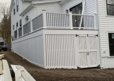 A white house with custom carpentry featuring a raised deck with railings and a panel enclosure.