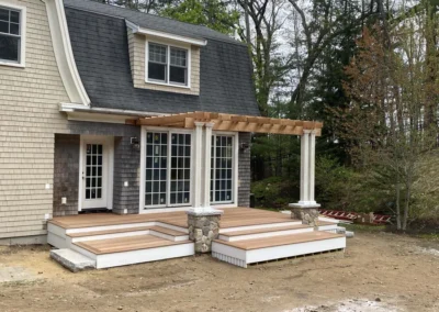 A custom-built wooden deck with a pergola attached to a house, featuring columns and stone bases.