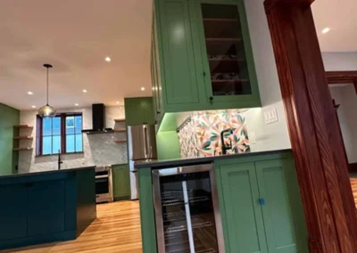 Modern kitchen interior with green cabinets, hardwood floors, and colorful backsplash