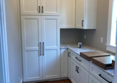 A custom carpentry kitchen setup featuring white cabinets with black handles and a marble countertop.