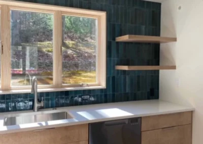 Modern kitchen with custom cabinetry, white countertop, blue tiled backsplash, and floating shelves.