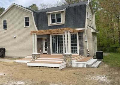 A two-story house with a wooden pergola and stone accents on the porch in a backyard setting.