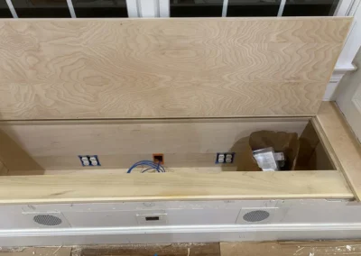 Custom carpentry storage bench with electrical outlets and wiring, placed under a window.