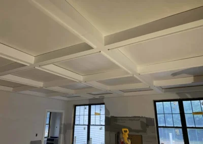 Room with custom coffered ceiling under construction, featuring painted white beams and recessed panels.