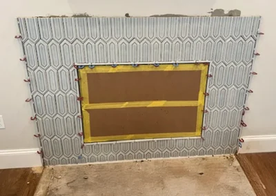 Tiled fireplace with hexagonal pattern, cardboard center taped in yellow, clamps around edges, missing tiles at bottom.