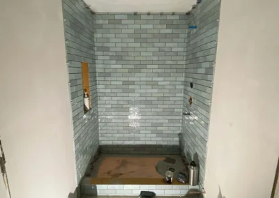 Bathroom under construction with light blue subway tiles installed in the shower area.