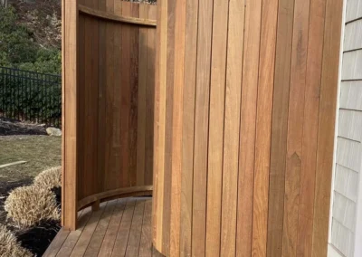 Outdoor wooden shower with curved design attached to house