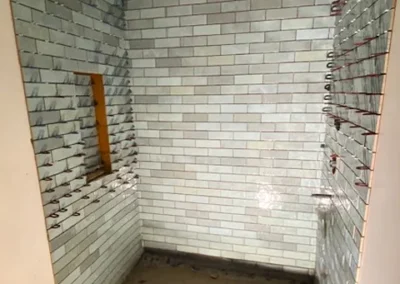 Shower stall with light gray subway tiles, unfinished with some wires protruding from the walls.