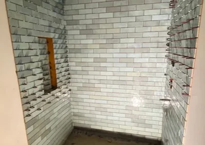 Partially tiled shower area with light blue subway tiles and thin plastic spacers between them.