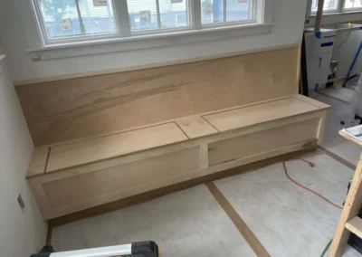 Custom wooden bench with storage underneath, located by a window in a room under construction.