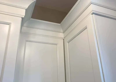 Interior view of custom carpentry crown molding and cabinetry with white finish.