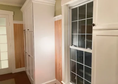 White cabinets and window with grid panes in a room with wood paneling and a glass door.
