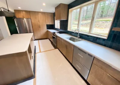 Modern kitchen with wood cabinets, white countertops, stainless steel appliances, and large windows.