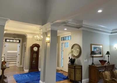 Interior view of an elegant room featuring custom carpentry with intricate crown molding, a grand chandelier, and a prominent grandfather clock.