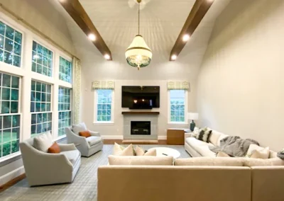 Spacious living room with vaulted ceiling, exposed wooden beams, large windows, a chandelier, and modern seating arrangement around a fireplace.