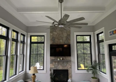 Sunroom featuring large windows, stone fireplace, ceiling fan, and elegant trim work.