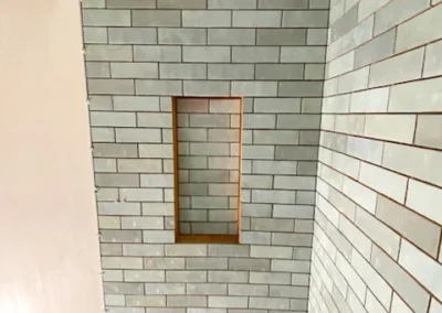 Gray tiles installed on two walls, with a narrow inset shelf on one wall.