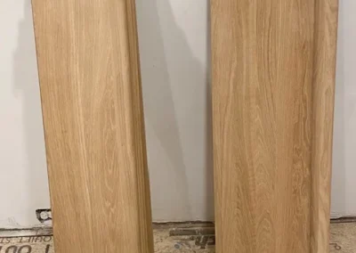 Two stacks of wooden panels leaning against a white wall.