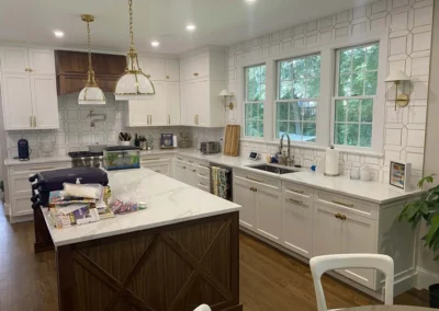 Modern kitchen with white cabinets, marble countertops, and wood accents featuring two hanging pendant lights.