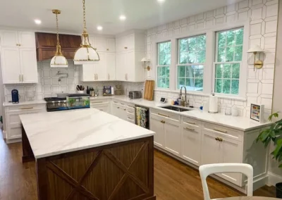 Modern kitchen with custom carpentry, featuring a large island with wooden accents, white cabinets, modern light fixtures, and a large window.