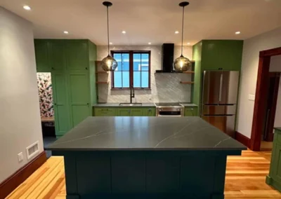 Modern kitchen interior with green cabinetry, a large dark-colored island, and wooden flooring.