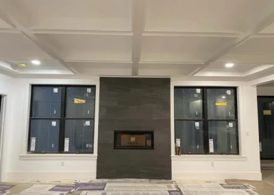 Interior view of a modern room featuring a coffered ceiling and a stone fireplace flanked by two large windows.
