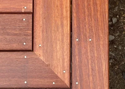 Close-up of a wooden deck corner with precise carpentry showing a miter joint and evenly spaced nails.