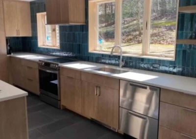 Modern kitchen with wooden cabinetry, teal wall tiles, and large windows.