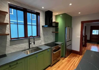 Modern kitchen with green cabinetry, stainless steel appliances, and wooden flooring.